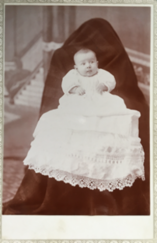 Victorian photograph of a baby in a white dress held by a person hidden with a black sheet