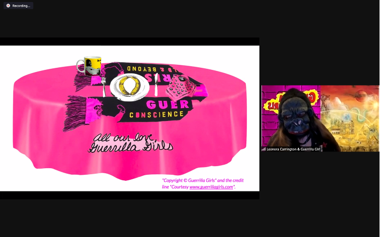 Fig. 9. Taylor Fennell, Guerilla Girls Virtual Presentation with Place Setting. This image depicts a screenshot of a Zoom presentation. On the left is a white box containing an image of a pink tablecloth on a round table. On the table is a black-and-pink scarf , a silver fork and knife, and a plate with two bananas. On the upper-left is a yellow mug. The tablecloth contains the following phrase, written in cursive: “All our love, Guerrilla Girls.” On the right is an image of a student wearing a gorilla mask against a pink brick backdrop and another backdrop containing a design in yellow and red.