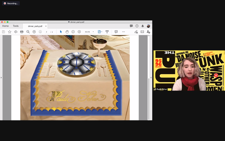 Fig. 10. Haley Romansky, Paula Scher Virtual Presentation with Place Setting. This image depicts a screenshot of a Zoom presentation. On the left is an image of a white table. On the table is a tablecloth bordered in blue and yellow, with the name “Paula Scher” written in gold scroll lettering. The table contains a plate with a black, yellow, and blue design, as well as a white fork and napkin (to the left of the plate) and knife and spoon (to the right of the plate). In the upper right-hand corner
is a silver wine glass. To the right of the place setting is a Zoom window in which we see a student, wearing a red scarf and white sweater. The student’s name is labeled as “Paula Scher.” The background is yellow with black, red, and white text. One of the visible phrases is “Bring in ’Da Noise.”