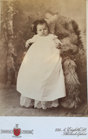 Victorian photograph of a baby in a white dress held by a person hidden with a rug
